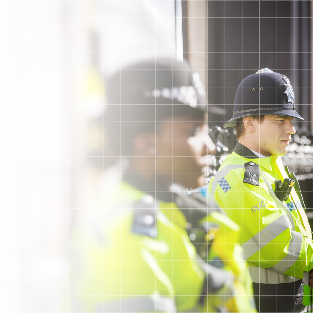 Two police officers in high-visibility jackets and traditional British helmets standing in profile.