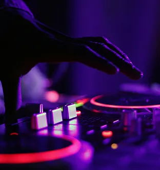 Hand adjusting controls on a DJ mixer illuminated with purple and red neon lights.