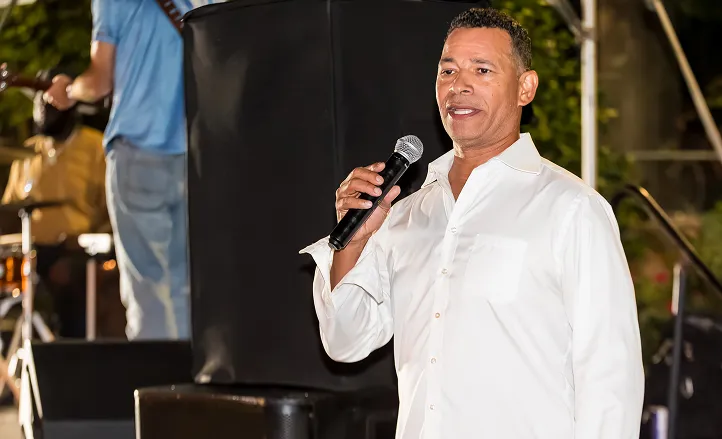 Man in white shirt holding a microphone speaking at an outdoor event.