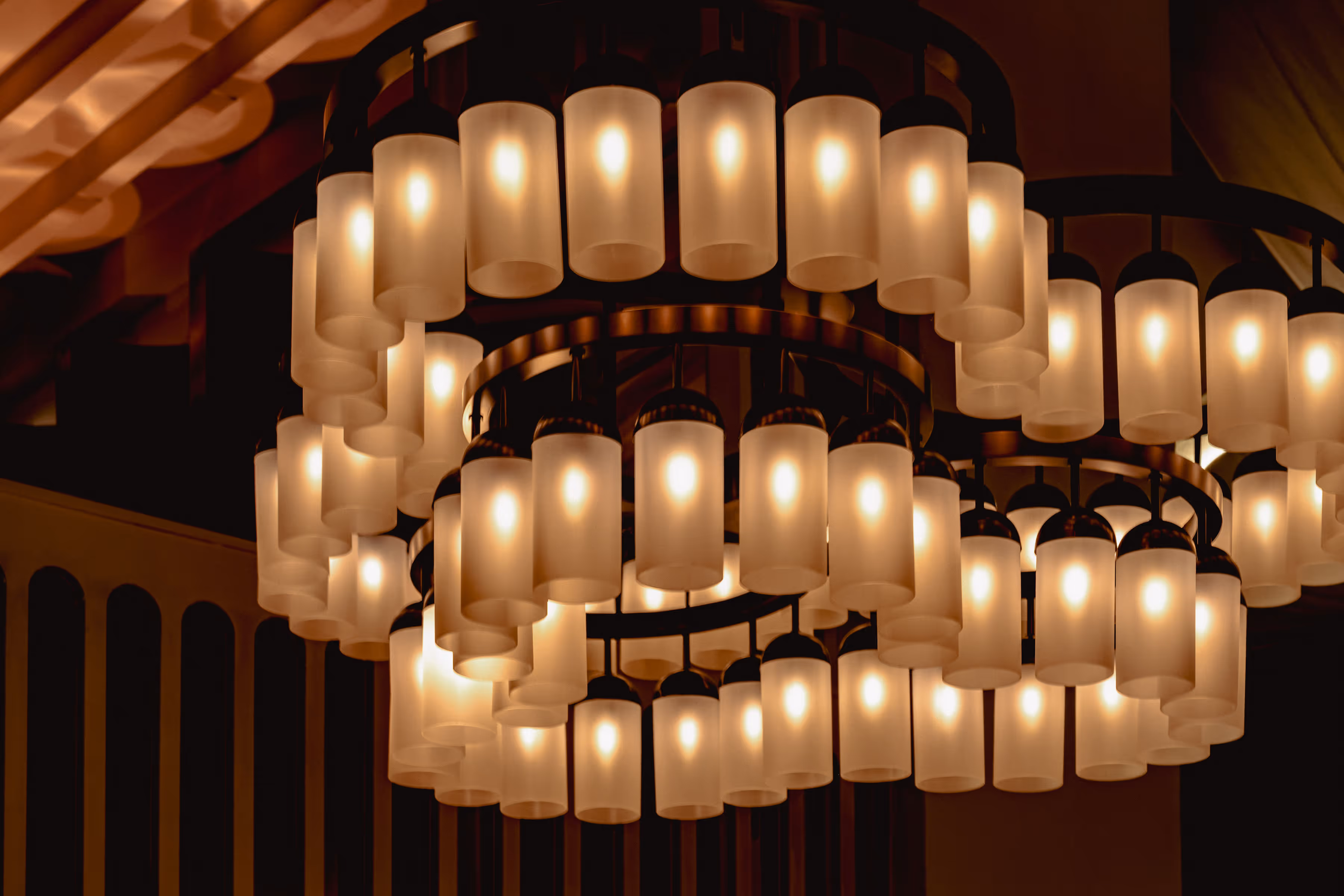 Circular chandelier with multiple cylindrical frosted glass lamps emitting warm light.