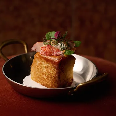 Petit gâteau salé carré garni de fruits de mer, de crème et garni de micropousses sur un petit moule en métal à anses.