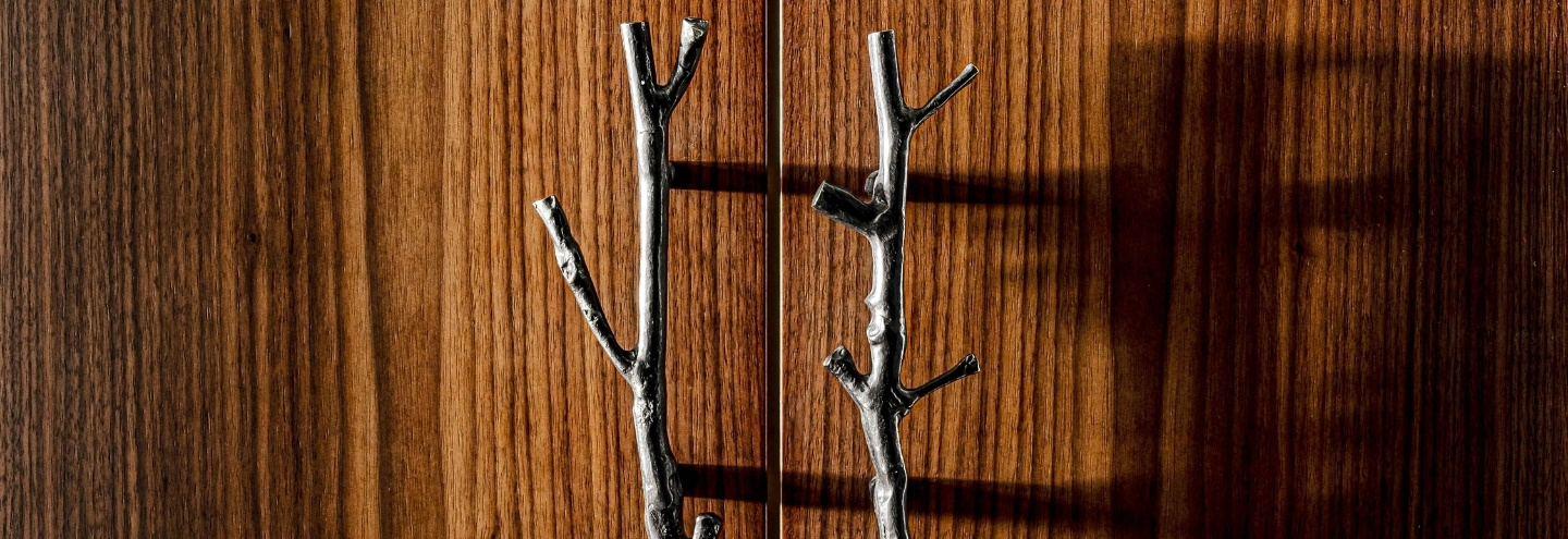 Gros plan de deux poignées de porte argentées en forme de branche sur une porte en bois à grain vertical.