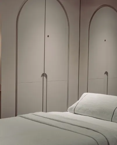 Minimalist room with arched wall panels and a neatly made bed with white linens and pillow.
