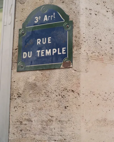 Blue and green Paris street sign mounted on a stone wall reading '3e Arrt RUE DU TEMPLE'.