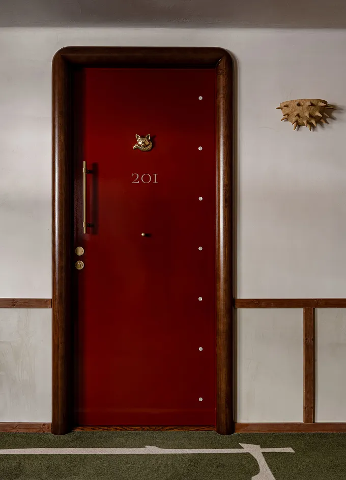 Dark red hotel room door numbered 201 with brown rounded frame and a gold cat-shaped door knocker.