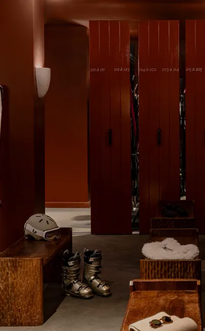 Ski locker room with wooden benches, ski boots, helmet, and lockers with room numbers.
