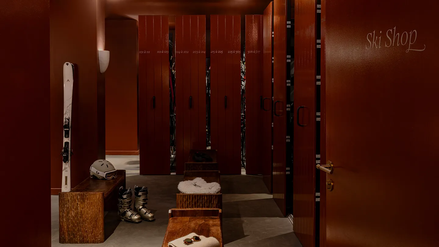Cozy ski shop interior with ski equipment, wooden benches, and brown lockers under warm lighting.