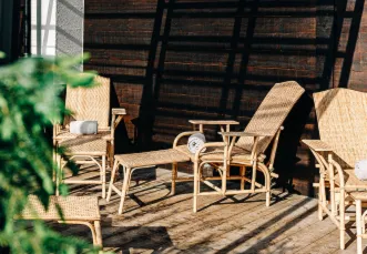 Wicker outdoor lounge chairs with cushions and a matching footrest on a wooden deck with sunlight and shadows.