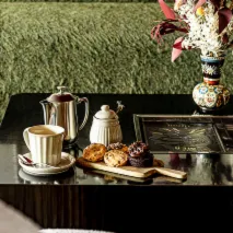 Table set with a cup of coffee, teapot, sugar bowl, two pastries, and a decorative vase with flowers.