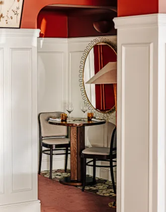 Cozy corner table set for two with chairs, wine glasses, and drinks in a restaurant with white paneled walls and a red ceiling.
