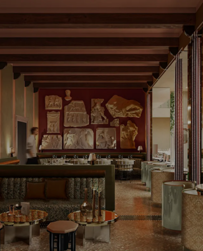 Luxurious hotel lounge with green velvet sofas, mosaic floor, and classical relief sculptures on red wall.