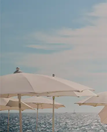 White beach umbrellas along the shore with a calm sea and a partly cloudy sky in the background.