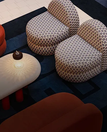 Two rounded patterned armchairs and a white table with a lit small lamp on a dark blue carpet.