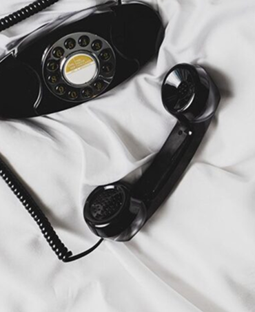 Black rotary dial telephone with the handset resting beside it on white fabric.