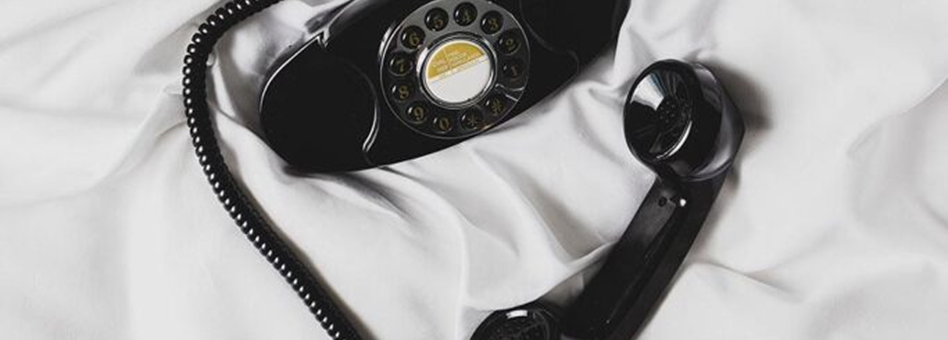 Black rotary dial telephone with handset off the cradle lying on white fabric.