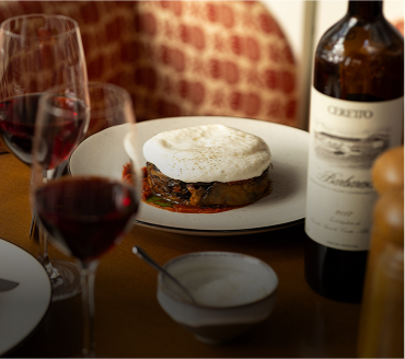 Plate with layered dish topped with foam, accompanied by a wine bottle and glasses of red wine on a table.