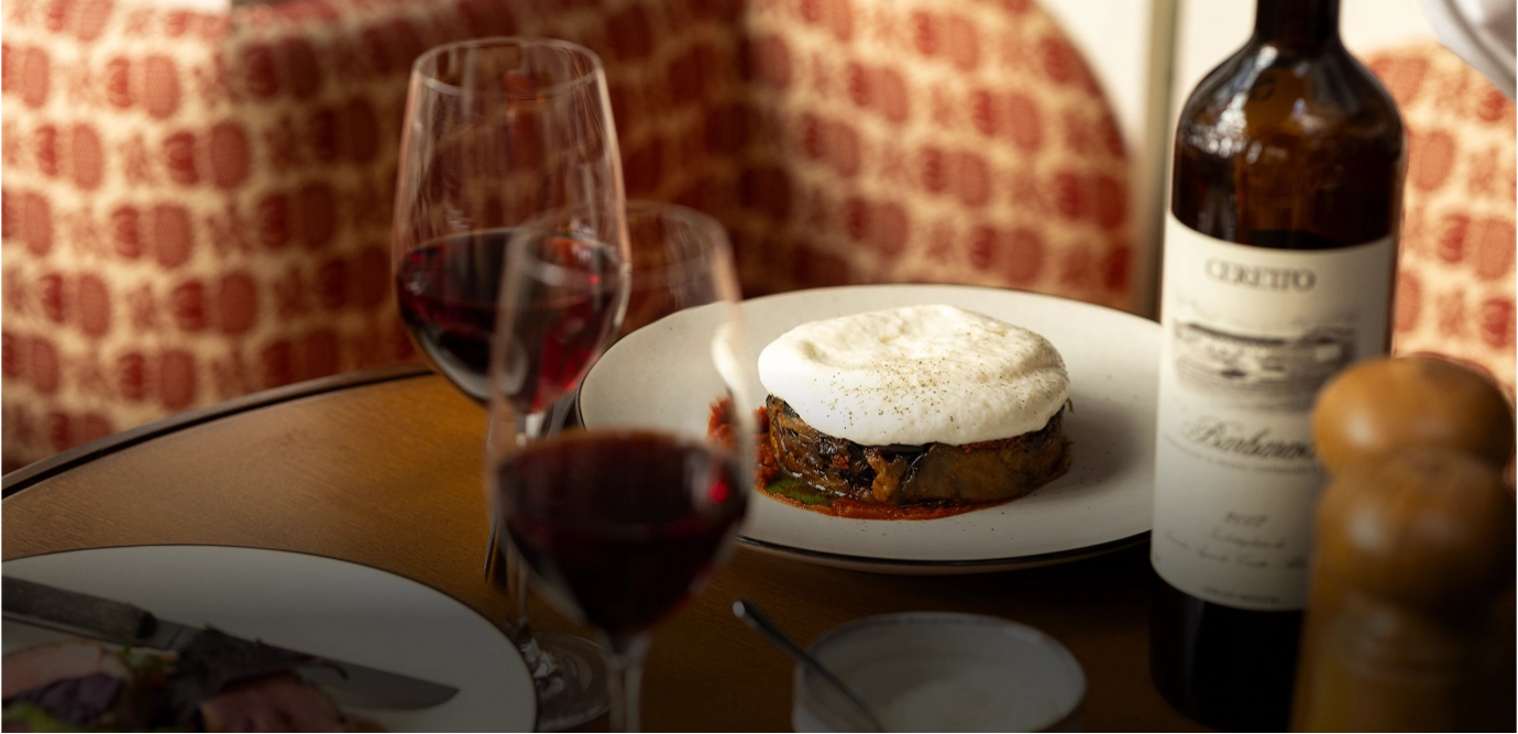 Table set with a gourmet layered dish topped with foam, two glasses of red wine, and a bottle of Ceretto Barbaresco wine.