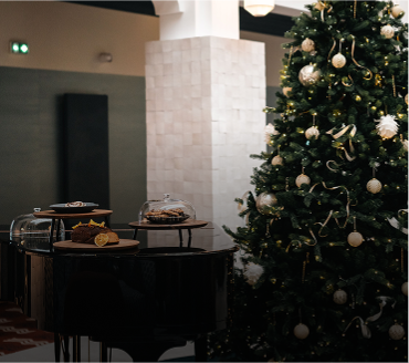 Black grand piano with assorted desserts on top next to a decorated Christmas tree with lights and ornaments.