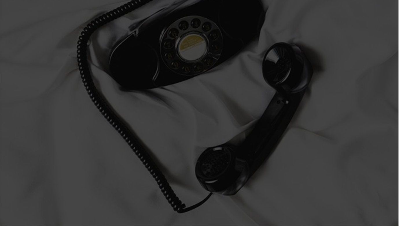 Black rotary dial telephone with handset resting on a white fabric surface.