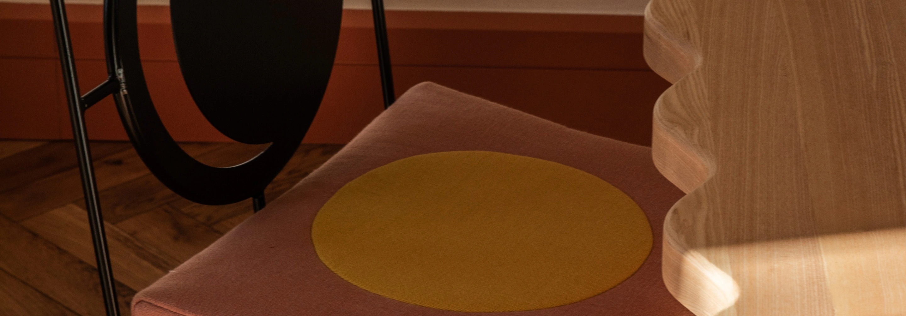 Close-up of a chair with a pink cushion featuring a large yellow circle, next to a wooden table with a wavy edge.