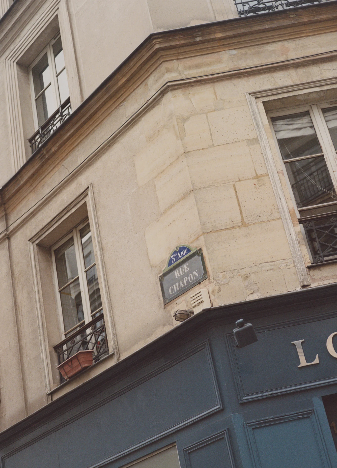 Corner of a Parisian building with a street sign reading 'Rue Chapon' in the 3rd arrondissement, beige stone walls, and windows with black wrought iron railings.