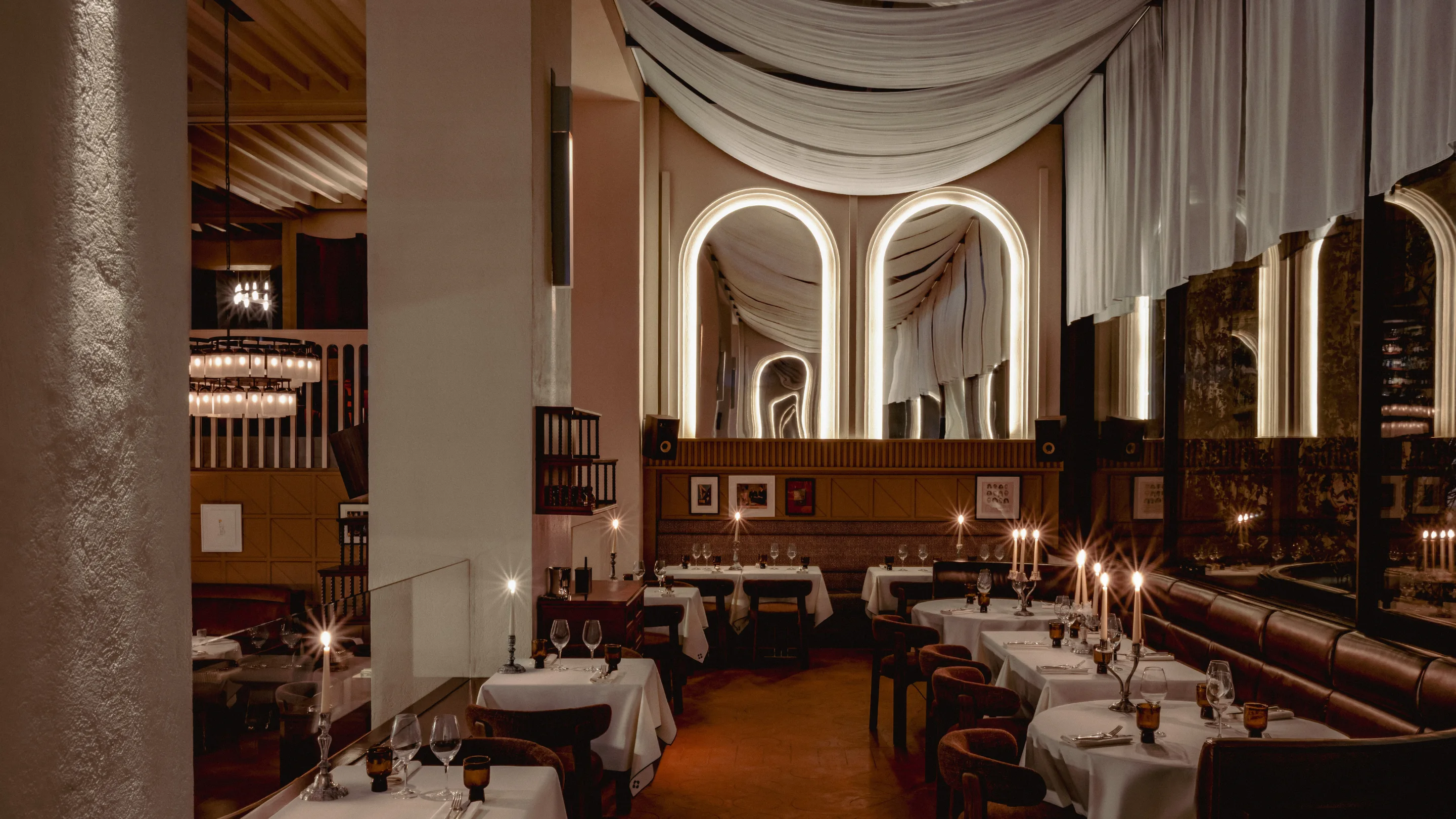 Elegant restaurant interior with candlelit tables, arched mirrors with soft lighting, and draped ceiling fabric.
