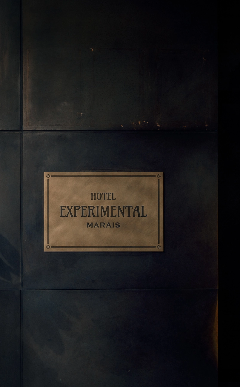 Plaque en bronze sur un mur sombre avec l'inscription « Hotel Experimental Marais ».