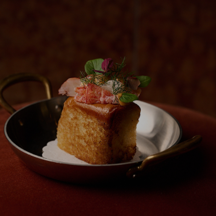 Pan tostado rectangular dorado cubierto con carne de langosta y hierbas verdes frescas en una sartén plateada con asas de latón.