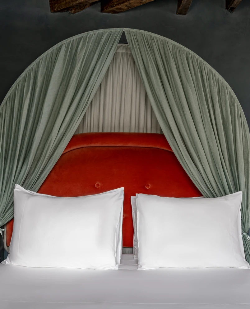 Bed with white pillows, red upholstered headboard, and green draped canopy in a hotel room.