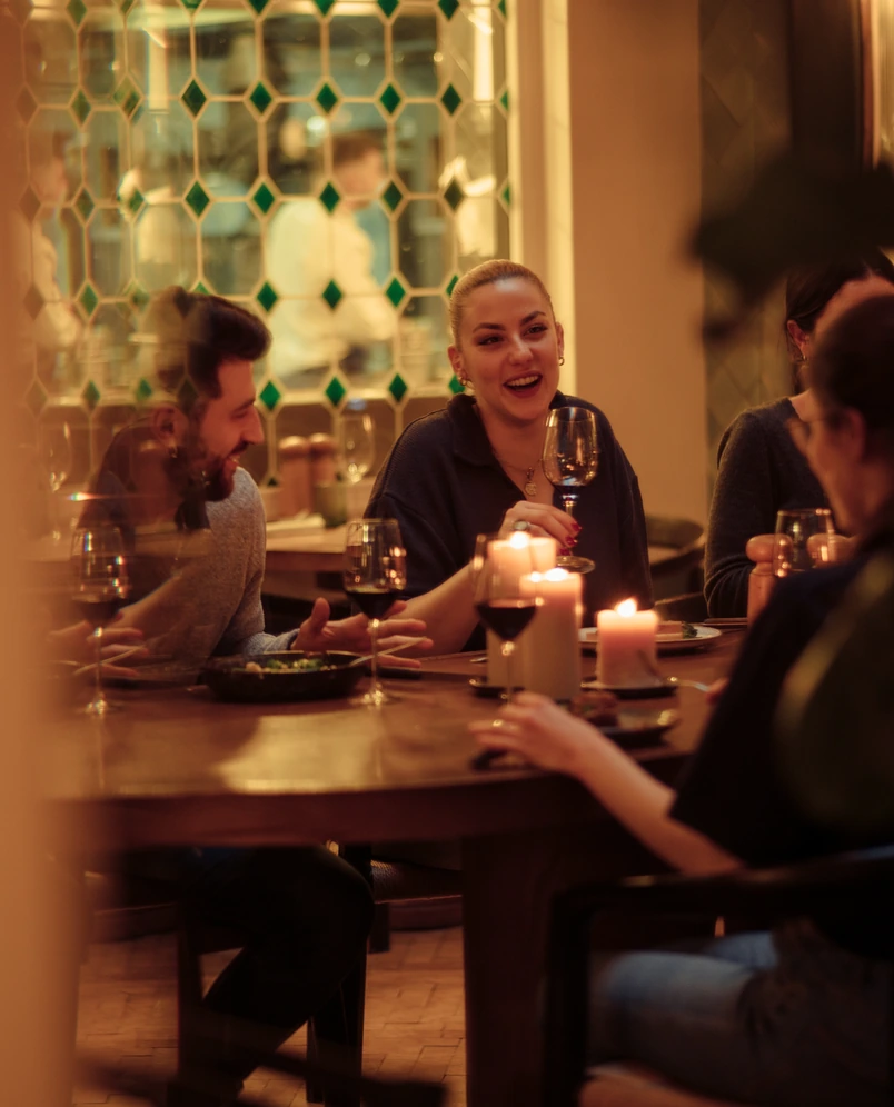 Group of friends enjoying a candlelit dinner with wine at a warmly lit restaurant.