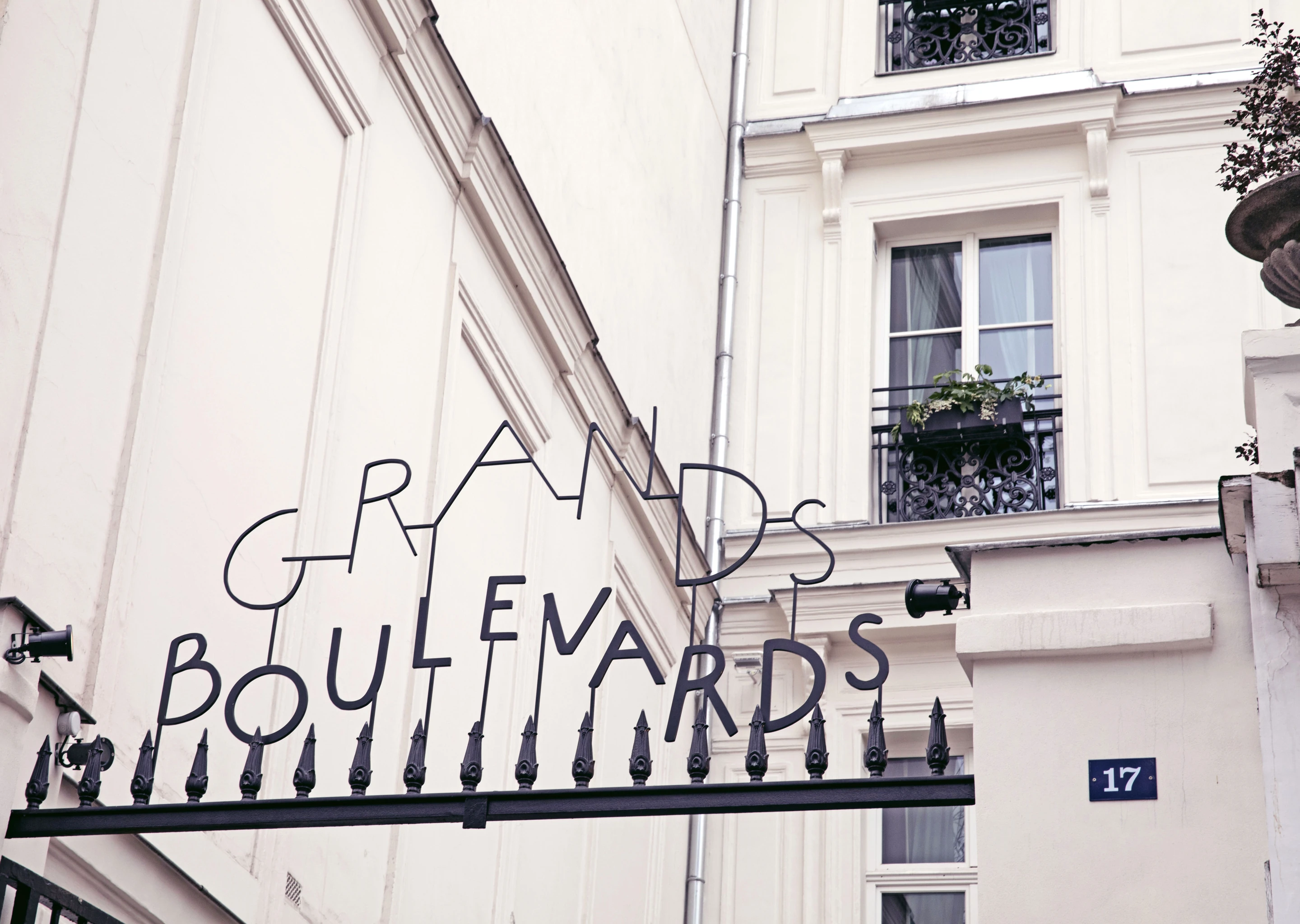 Black wrought iron sign reading 'Grands Boulevards' above a black gate in front of a white building with windows and a flower box.