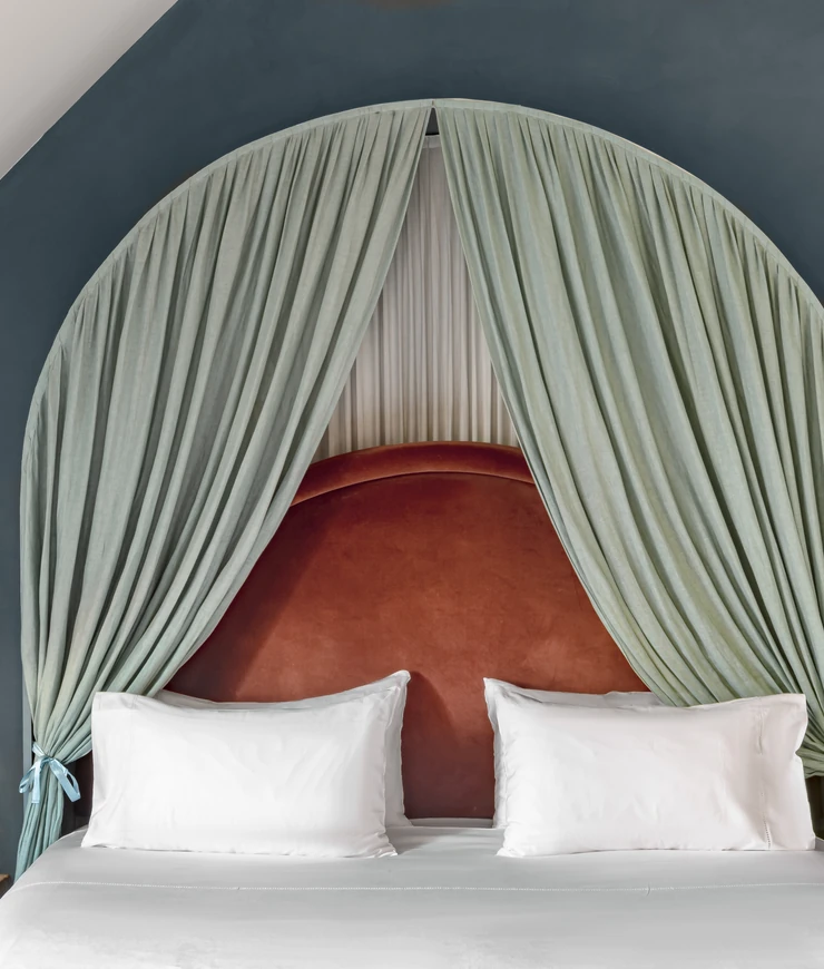 Luxurious bed with white pillows and sheets, set against a curved red headboard framed by light green curtains tied back in an arch shape.