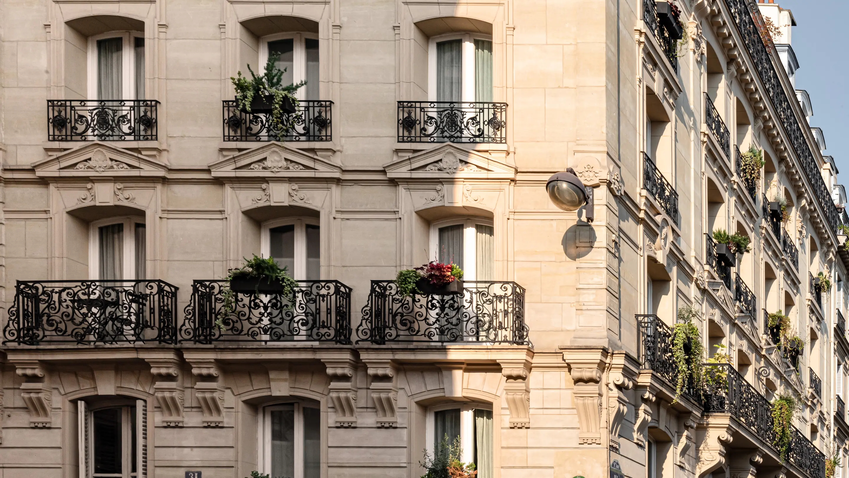 Edificio histórico de piedra beige con balcones ornamentados de hierro negro adornados con plantas y flores verdes.