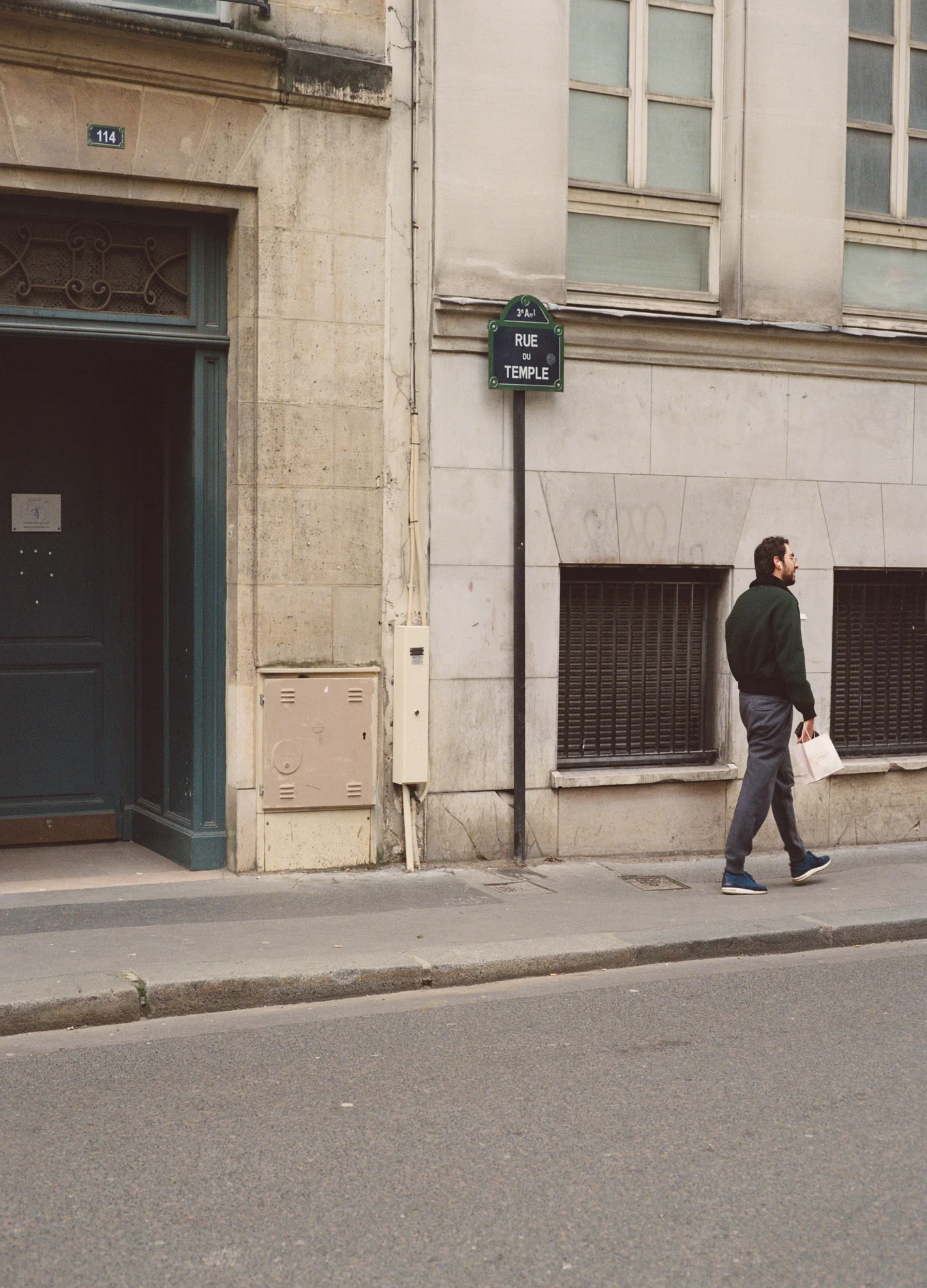 Un homme marche sur le trottoir devant un bâtiment en pierre beige avec un panneau indiquant la rue du Temple et le numéro 114 au-dessus d'une porte.