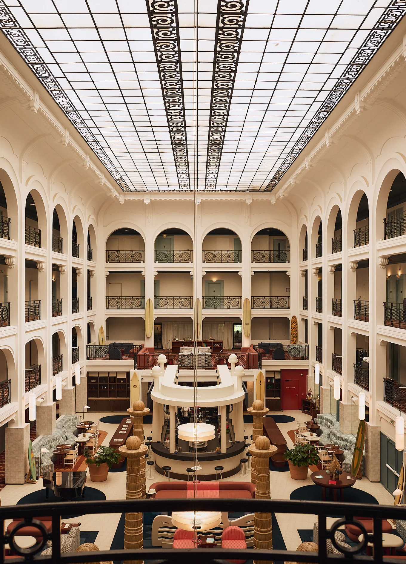 Spacious hotel atrium with arched balconies, a large skylight ceiling, seating areas, and a central bar.