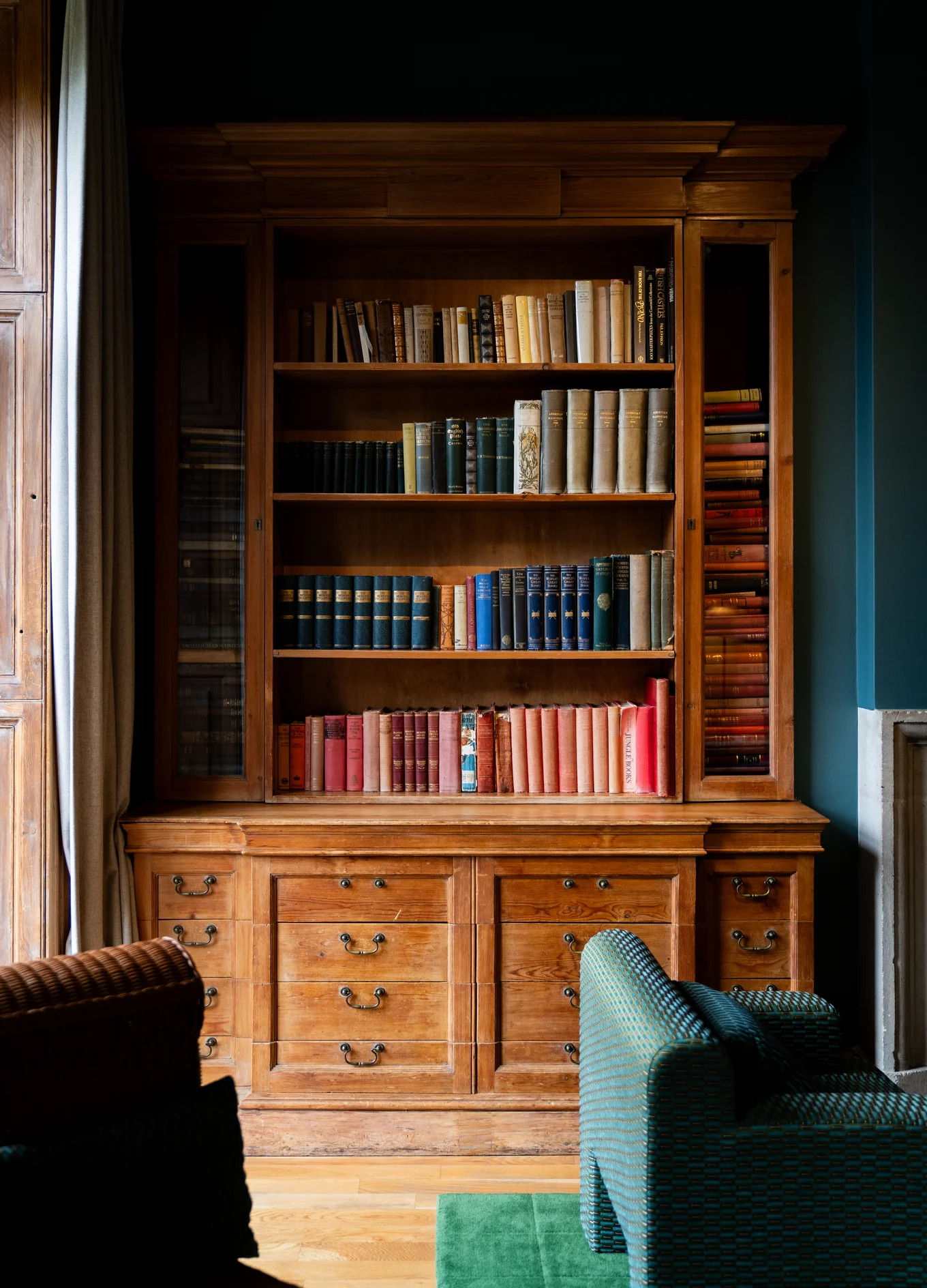 Wooden bookshelf filled with neatly arranged books in various colors in a cozy library setting.