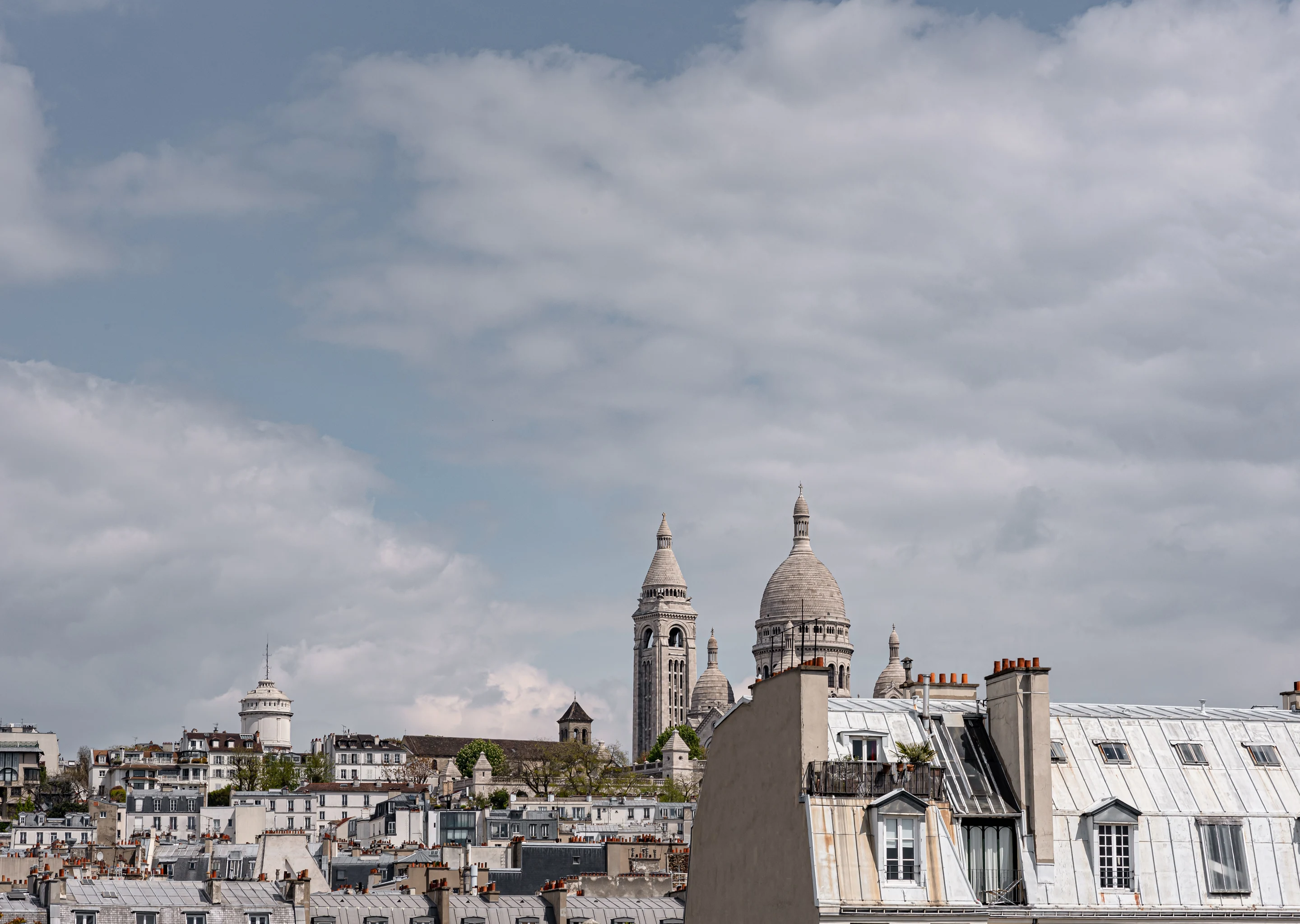 Los tejados de París con la basílica del Sagrado Corazón visible de manera prominente bajo un cielo parcialmente nublado.