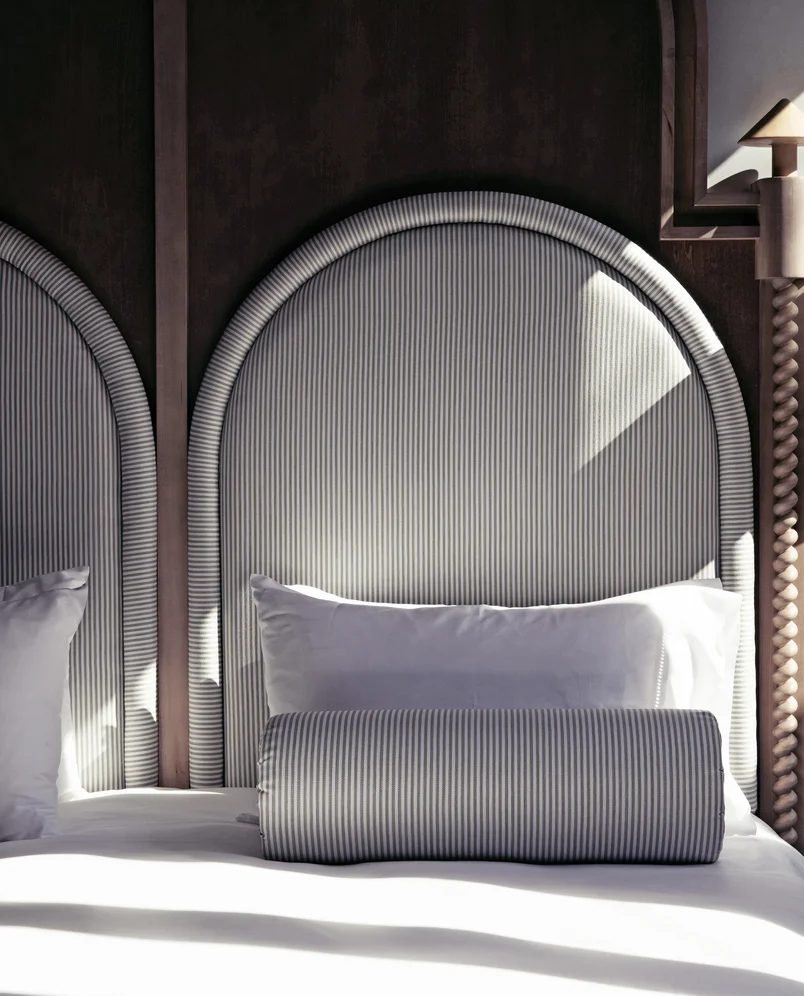 Close-up of a bed with a tall, rounded striped headboard, white pillows, and a matching cylindrical bolster pillow.