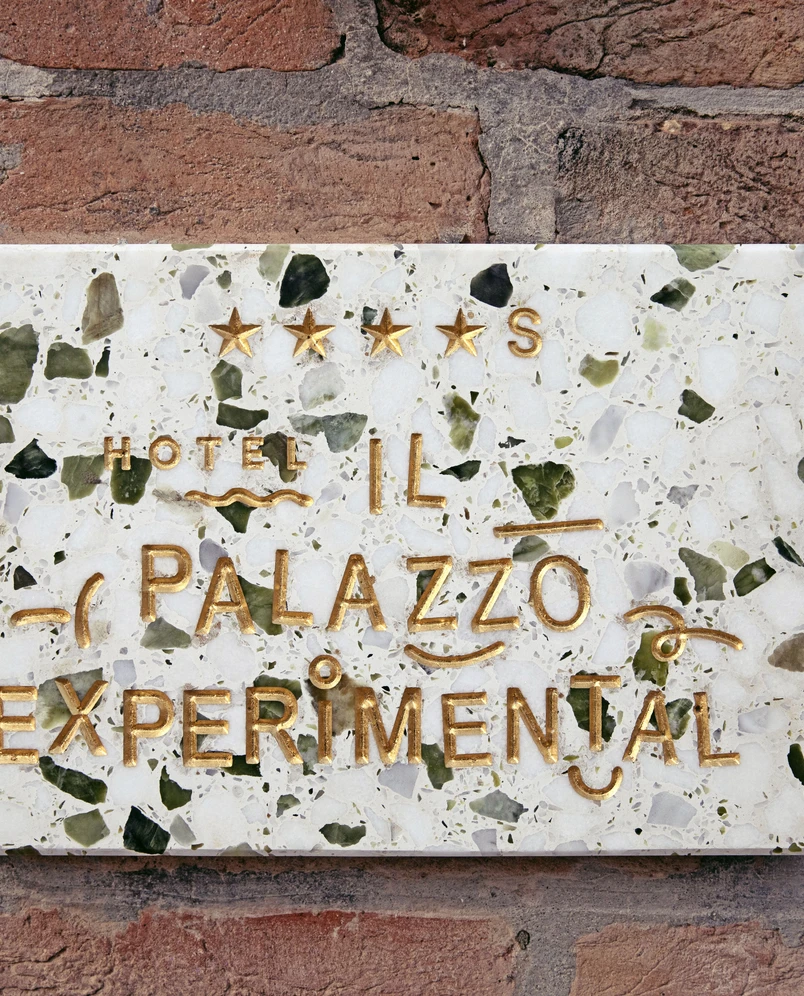 Marble plaque on brick wall with gold lettering reading 'Hotel Il Palazzo Experimental' and four stars.