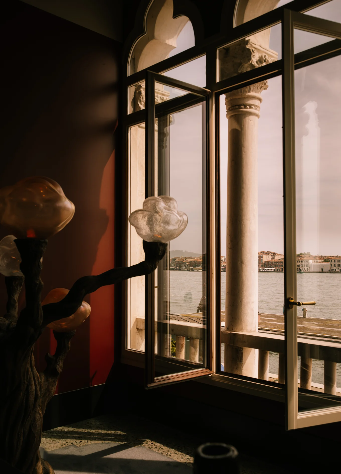 Open window with arched top and column frame overlooking waterfront buildings across calm water.