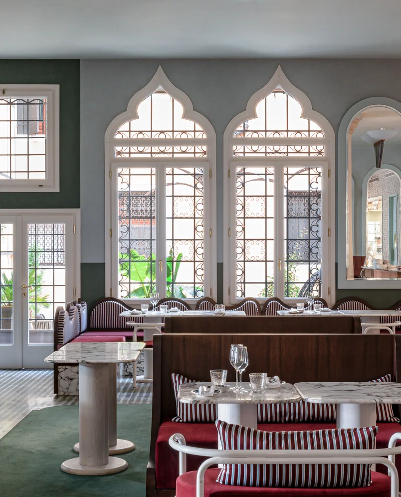 Elegant restaurant interior with arched windows featuring intricate wrought iron designs, marble tabletops, and red cushioned seating.