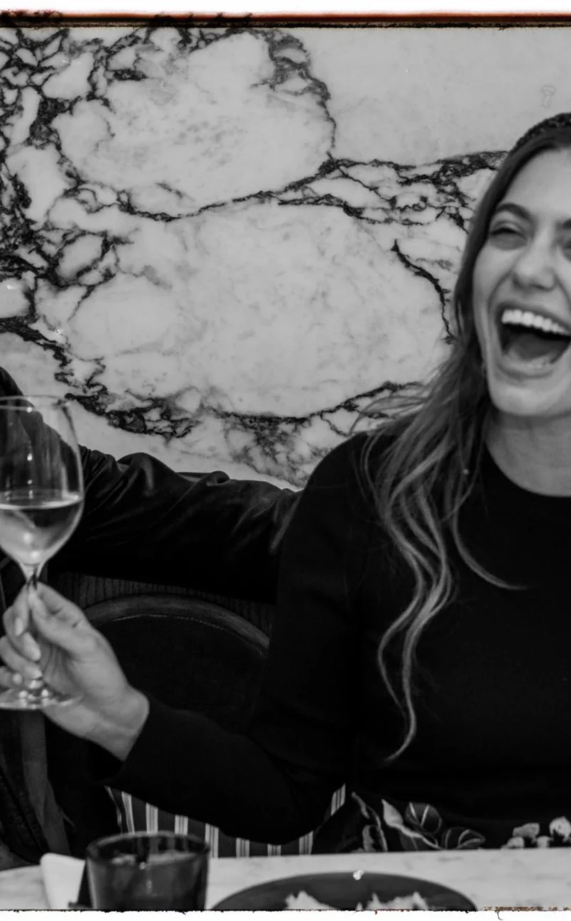 Woman laughing joyfully while holding a wine glass at a marble table.