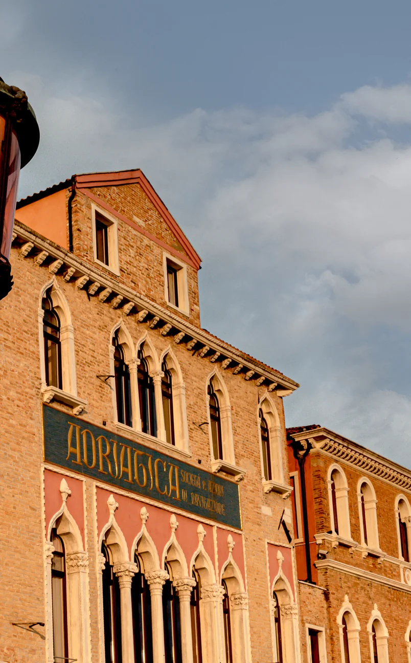 Historic brick building with arched windows and a sign reading 'Adriatica Soggiorni e Esercizi di Navigazione' under a partly cloudy sky.