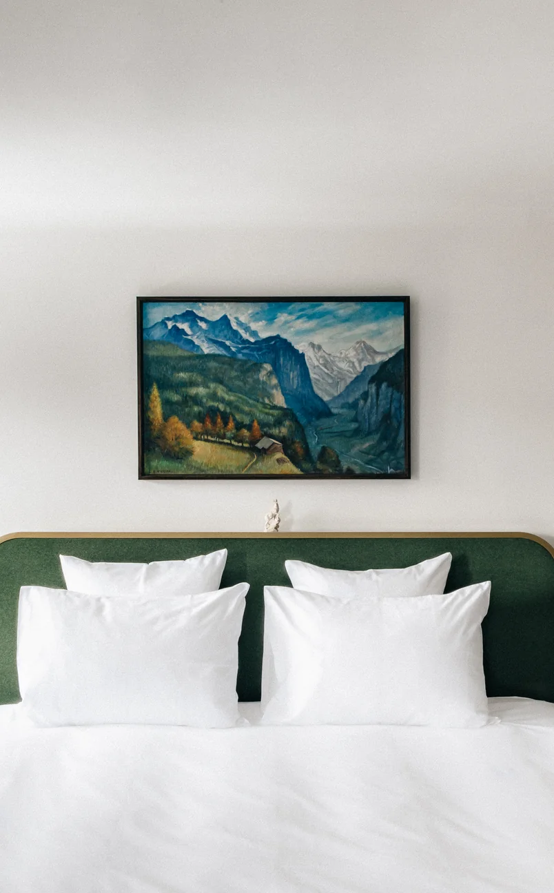 Bedroom with a green headboard, white pillows and bedding, and a framed mountain landscape painting above the bed.