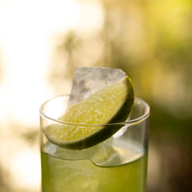 Glass of green citrus drink with ice and a lime wedge garnish.
