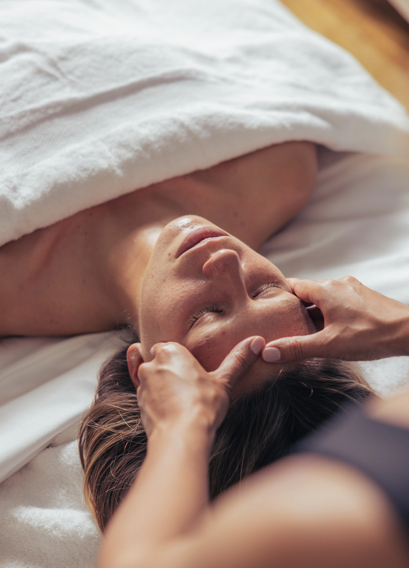 Person receiving a relaxing facial massage while lying under a white towel.
