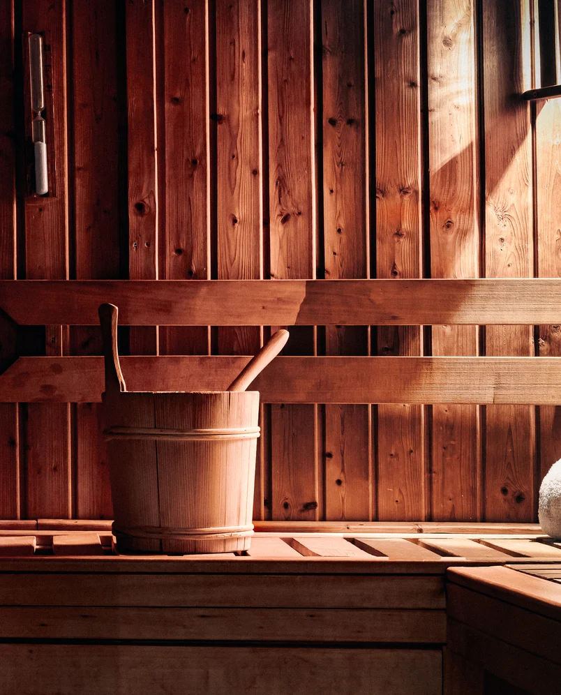 Wooden sauna interior with a bucket and ladle on a wooden bench.