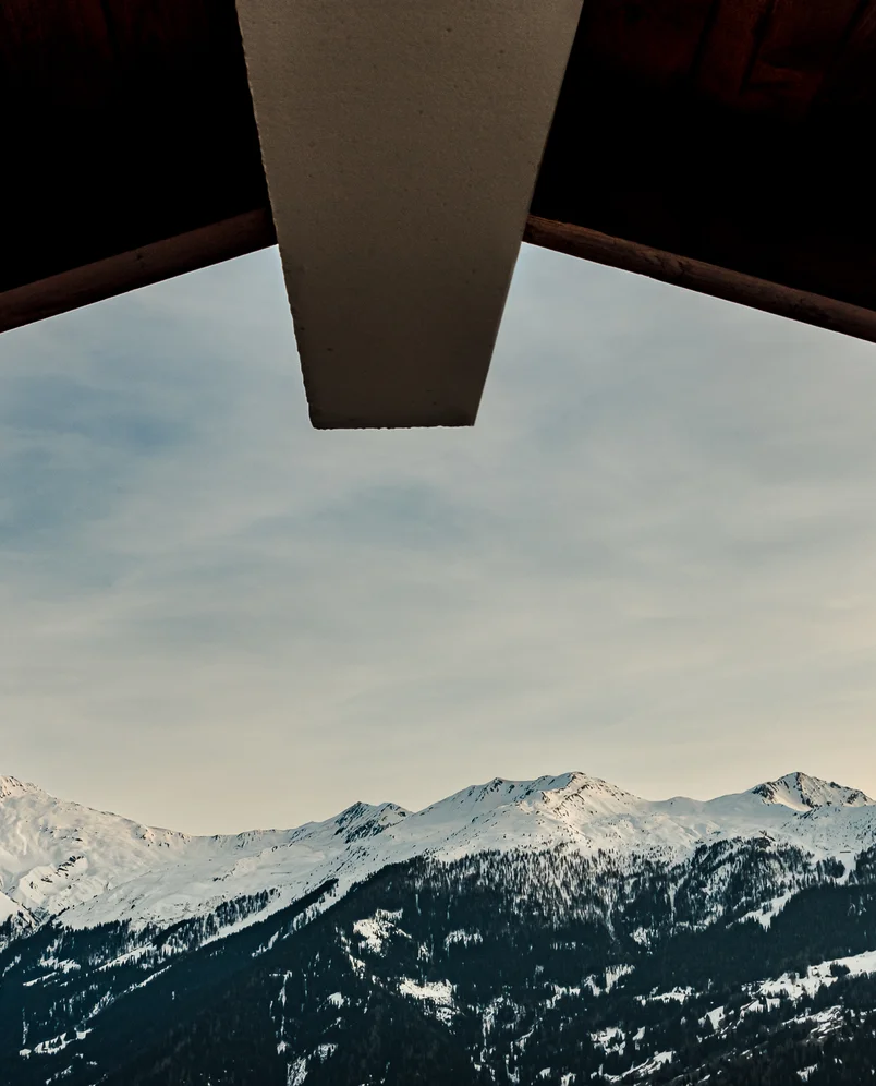 View of snow-covered mountain peaks under a cloudy sky framed by the dark roof of a building.