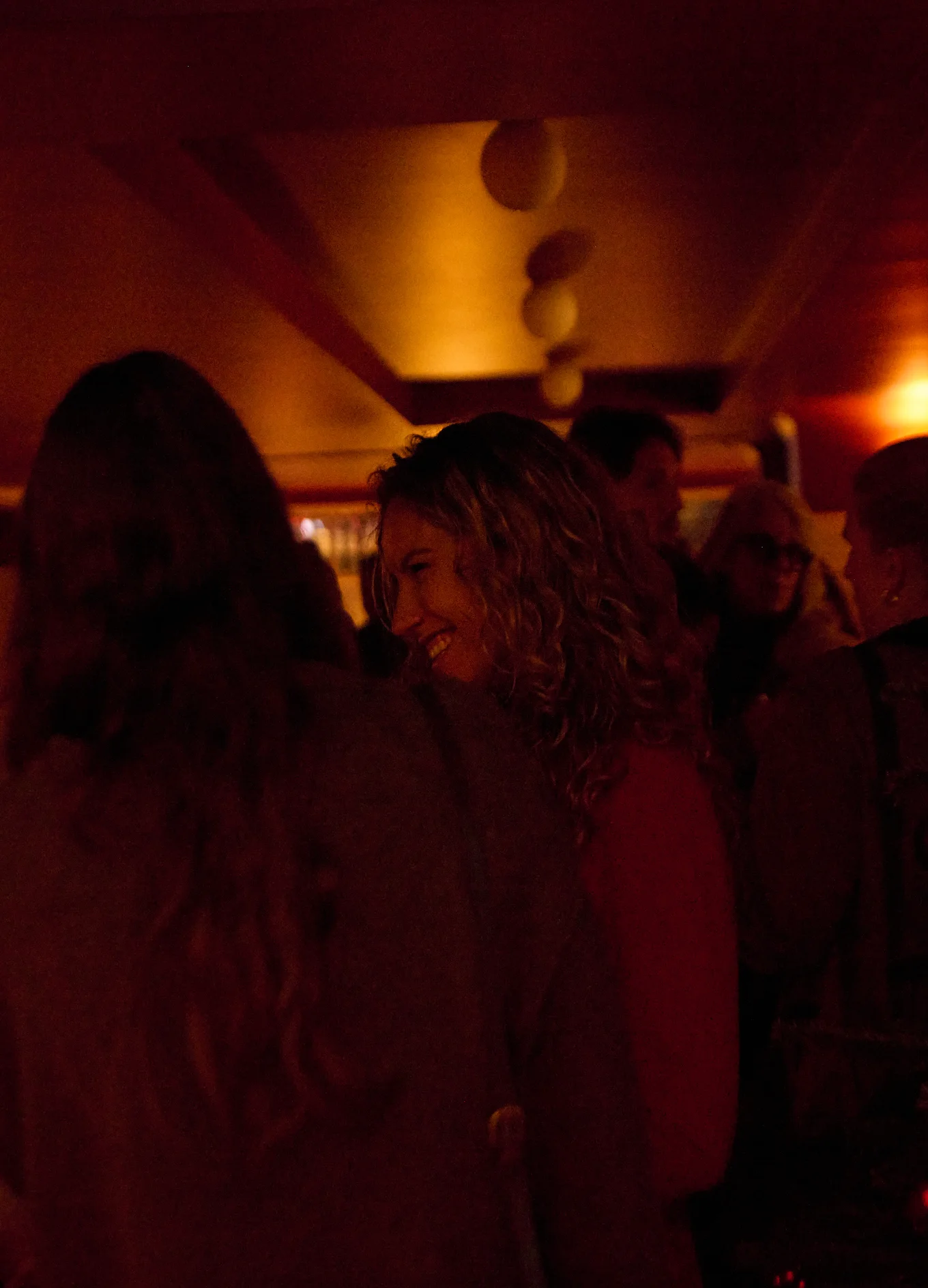 People socializing at a dimly lit indoor event with warm red and orange lighting.