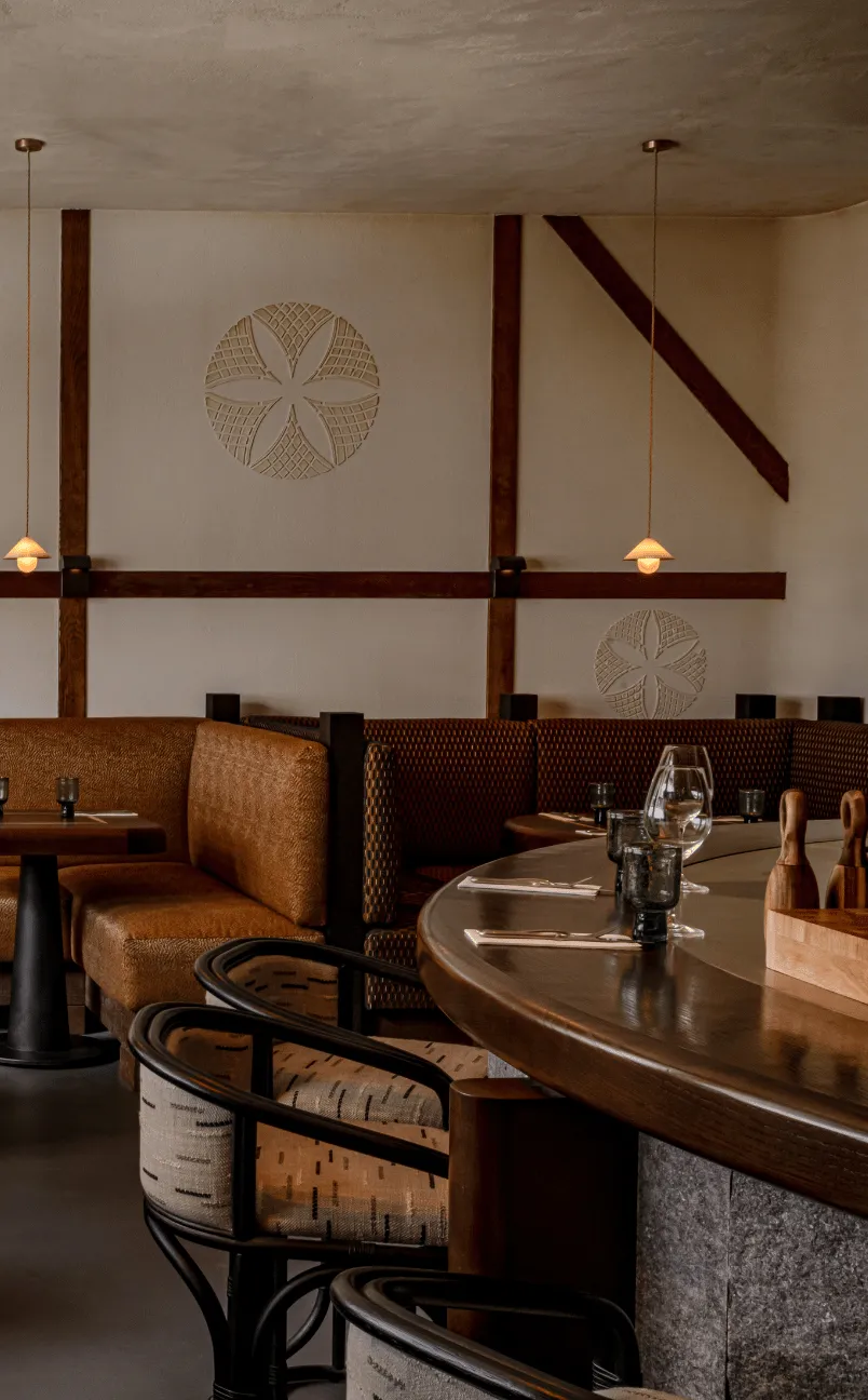 Cozy restaurant interior with brown leather booths, patterned chairs, wooden tables set with glasses and cutlery, and wall decorations.